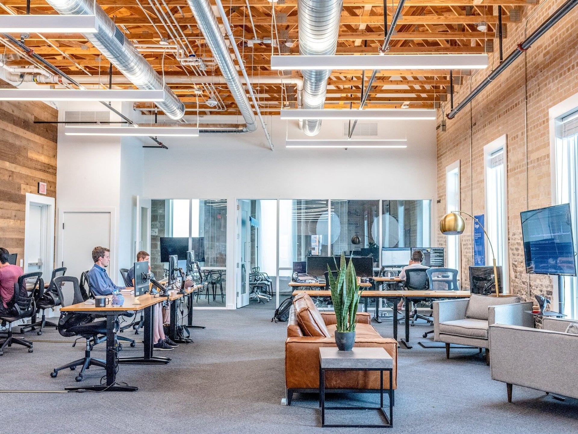A real working floor — teammates at desks along a brick wall in a bright open office with meeting rooms behind them