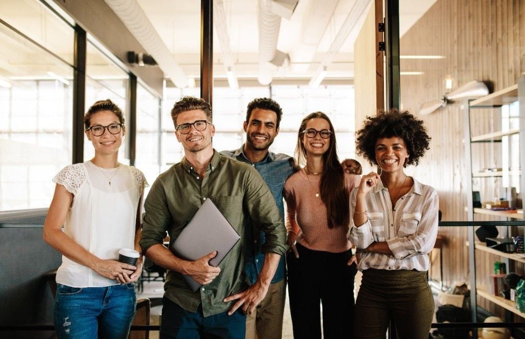 A group portrait of five Online VA Team teammates standing together — five teammates, one bench, one frame. The literal expression of 'Eighteen roles. One bench.'